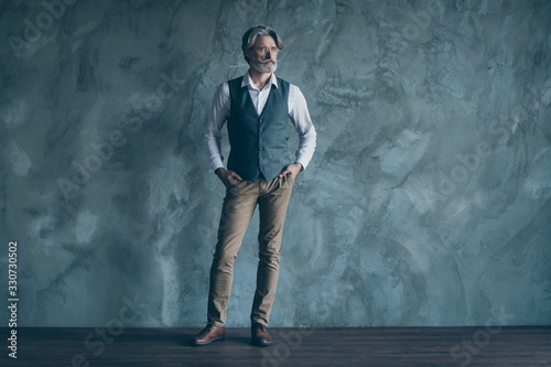 Full body photo of attractive mature business man neat beard hairdo seriously look side wear specs office shirt waistcoat pants isolated over concrete grey color wall background