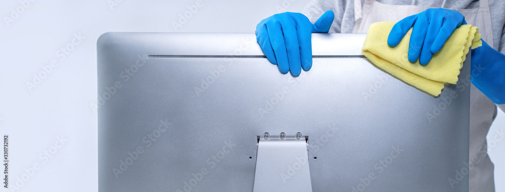 Young woman housekeeper in apron is doing cleaning silver computer screen with blue gloves, wet yellow rag, close up, copy space, blank design concept. - obrazy, fototapety, plakaty 