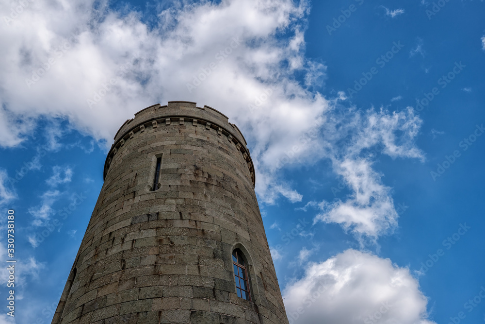 Stone castle tower with battlements and narrow windows with blue sky and white clouds background