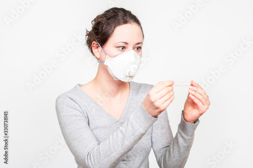 caucasian brunette woman in protective medical mask on face protection for spreading of disease virus SARS-CoV-2, Coronavirus, COVID-19. with mercury thermomether. white background photo