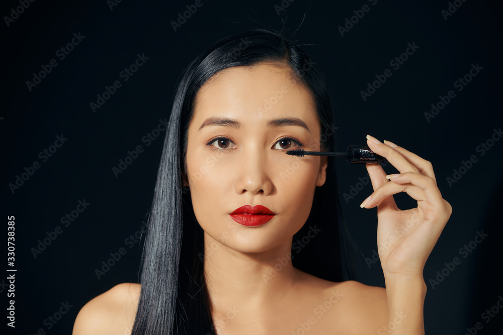 Close-up portrait of nice lovely cute sweet attractive cheerful positive Asian woman holding in hands applying trendy black mascara isolated