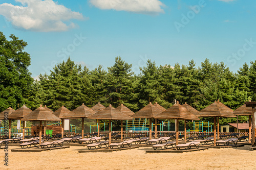 Sandy beach with brown wooden loungers and umbrellas. Empty rows resting places.