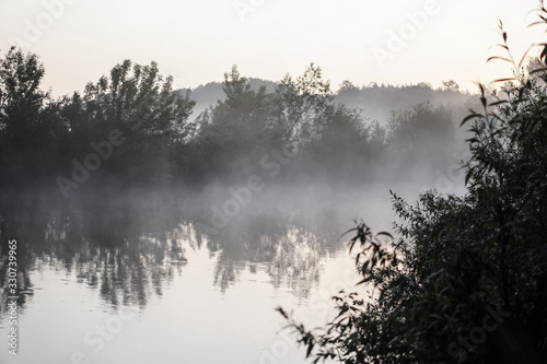 Beautiful morning river, a lake in light fog and the rays of the sun. Trees and bushes glow in the evening. Stock nature background for design.