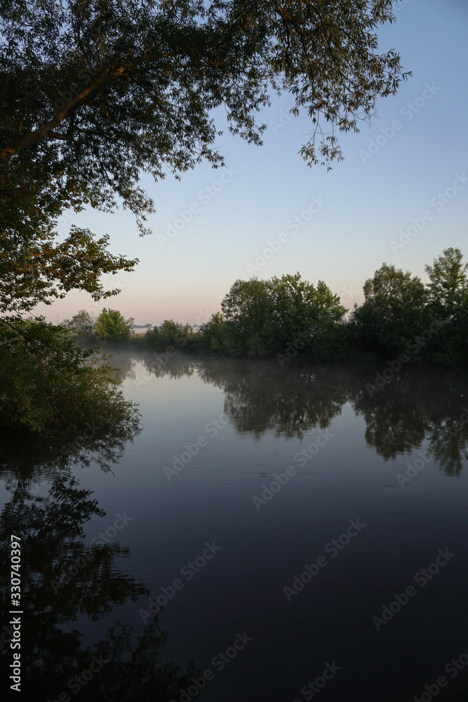 Beautiful morning river, a lake in light fog and the rays of the sun. Trees and bushes glow in the evening. Stock nature background for design. Beautiful morning river, a lake in light fog and the rays of the sun. Trees and bushes glow in the evening. Stock nature background for design.