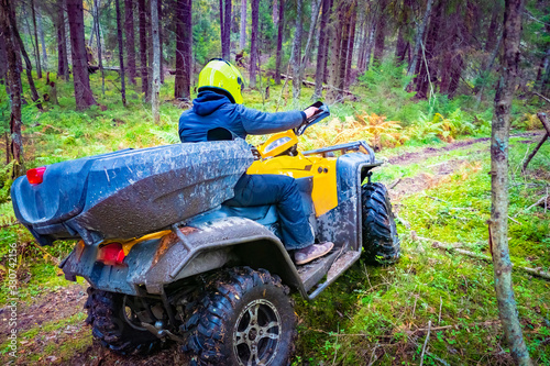 A man rides a Quad bike on a forest road. ATV ride through the forest. Racing on a forest road. Transport for hard-to-reach places. Extreme sport. A dirty Quad bike rushes through the forest.