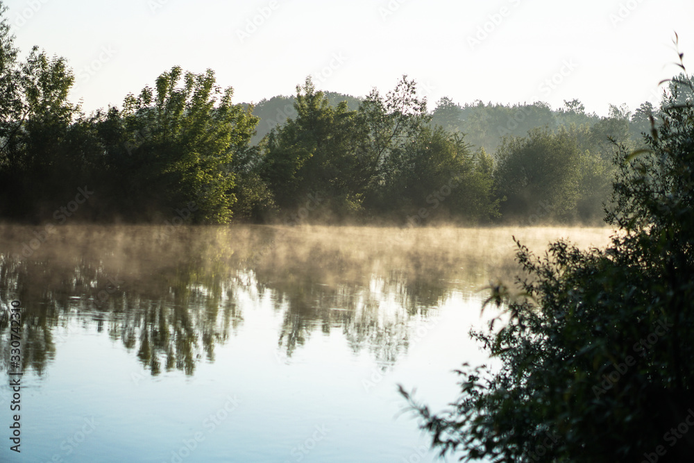 Beautiful morning river, a lake in light fog and the rays of the sun. Trees and bushes glow in the evening. Stock nature background for design. Beautiful morning river, a lake in light fog and the rays of the sun. Trees and bushes glow in the evening. Stock nature background for design.