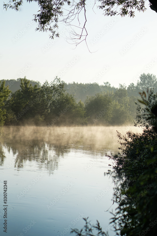 Beautiful morning river, a lake in light fog and the rays of the sun. Trees and bushes glow in the evening. Stock nature background for design. Beautiful morning river, a lake in light fog and the rays of the sun. Trees and bushes glow in the evening. Stock nature background for design.