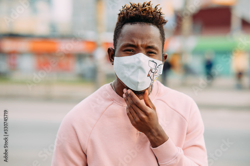 Portrait of young African man with a medical protective mask on his face at city street.