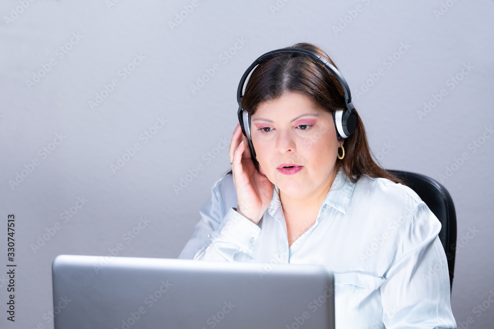 Business woman working on a computer in her office. She is looking at the laptop screen. She has long, smooth and dark hair. She is using headphones for a video conference call. Business woman working on a computer in her office. She is looking at the laptop screen. She has long, smooth and dark hair. She is using headphones for a video conference call.