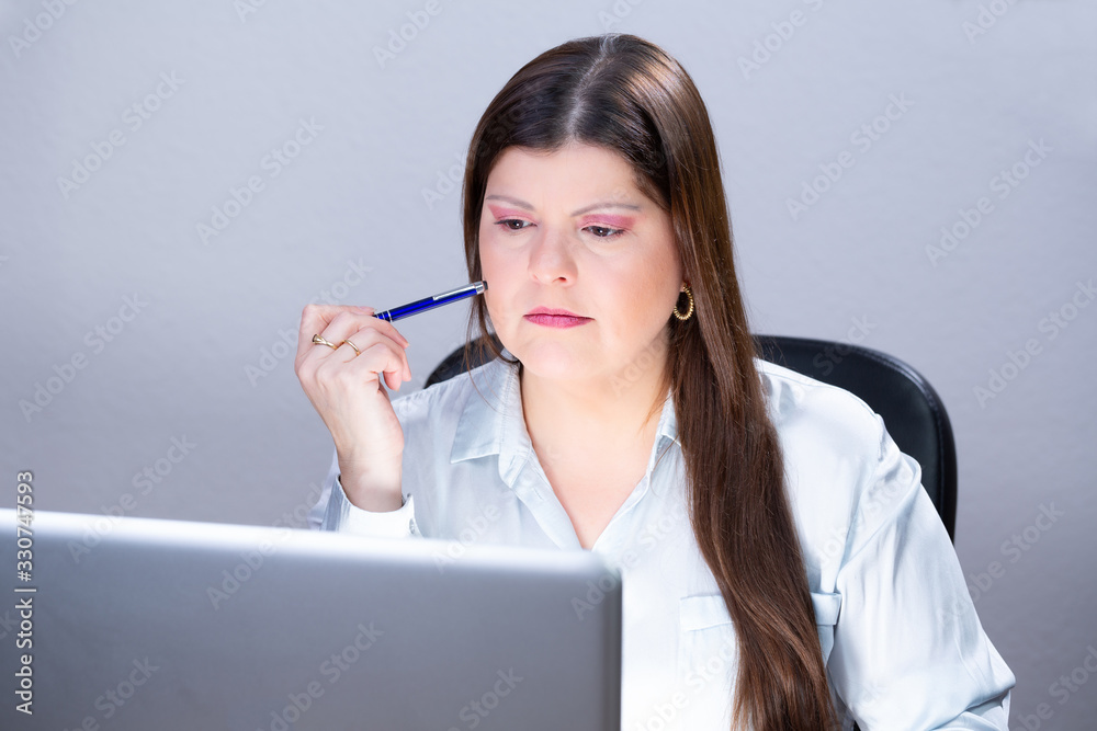 Business woman working on a computer in her office. She is serious and looking at the laptop screen. She has long, smooth and dark hair. She is caucasian in her late 30s. This is a studio portrait. Business woman working on a computer in her office. She is serious and looking at the laptop screen. She has long, smooth and dark hair. She is caucasian in her late 30s. This is a studio portrait.