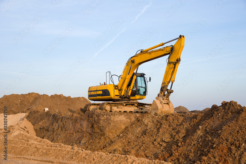 Excavator working at construction site. Backhoe digs ground for the foundation and for paving out sewer line. Construction machinery for excavating, loading, lifting and hauling of cargo on job sites Excavator working at construction site. Backhoe digs ground for the foundation and for paving out sewer line. Construction machinery for excavating, loading, lifting and hauling of cargo on job sites