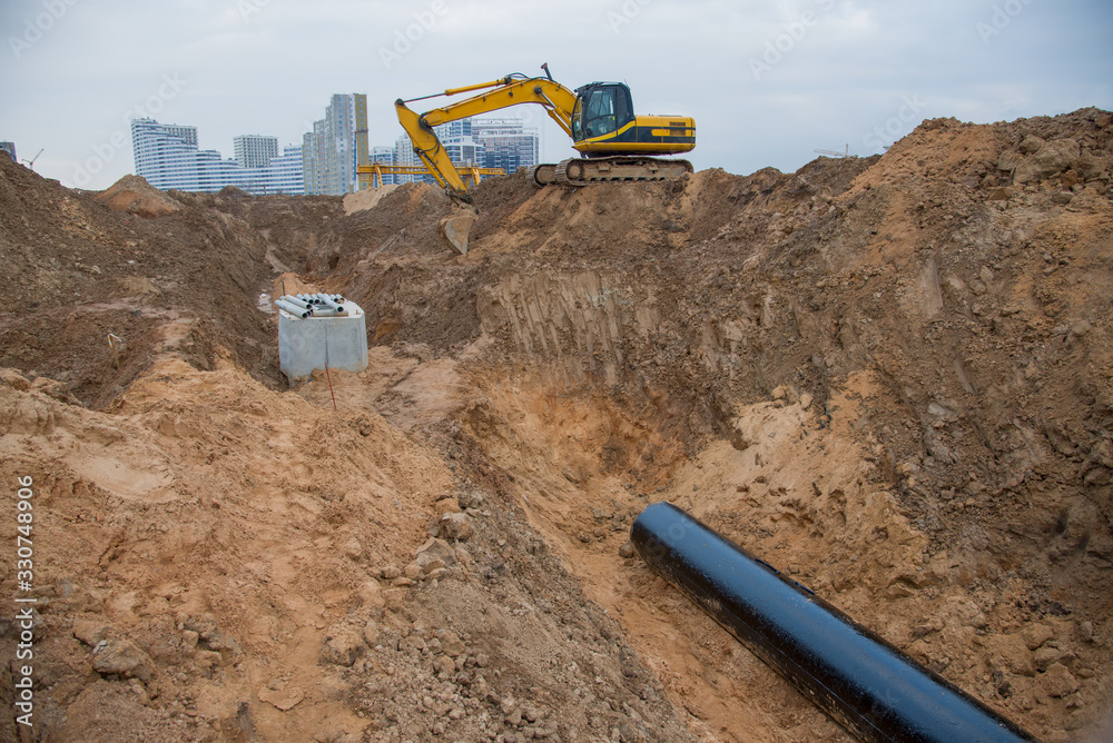 Excavator during laying drain pipes and concrete manholes for stormwater system. Connecting trench drain to concrete manhole at construction site. Construct stormwater and underground utilities Excavator during laying drain pipes and concrete manholes for stormwater system. Connecting trench drain to concrete manhole at construction site. Construct stormwater and underground utilities