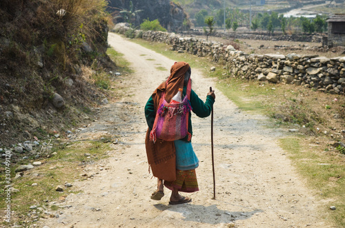 Señora anciana de espaldas caminando por un camino de piedra en el campo photo