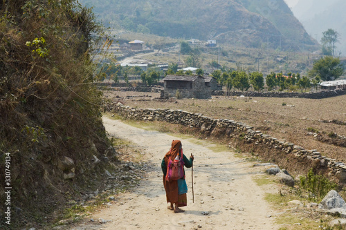 Señora anciana caminando en soledad por el campo con montañas al fondo photo