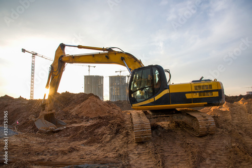 Excavator at earthworks on construction site. Backhoe loader digs a pit for the construction of the foundation. Digging trench for laying sewer pipes drainage in ground. Earth-Moving Heavy Equipment photo