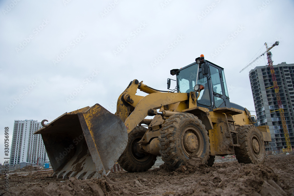 Fototapeta premium Front-end loader working at construction site. Earth-moving heavy equipment for road work. Public works, civil engineering, road building. Construction machinery for loading, lifting cargo