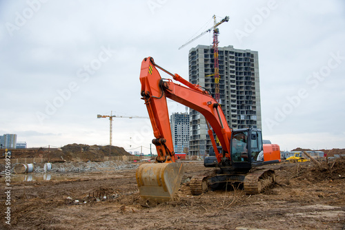 Excavator working at construction site on earthworks. Backhoe digs ground for the foundation and for paving out sewer line. Construction machinery for excavating, loading, lifting and hauling of cargo photo