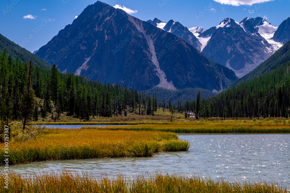 Forest lake on the background of snow-capped mountain peaks in the Altai Republic.