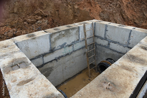 Valve pit for underground piping networks on construction site. Concrete manhole rings and valve chamber sewage pumping stations. Construct stormwater and underground utilities. Instaling sewers pipes © MaxSafaniuk