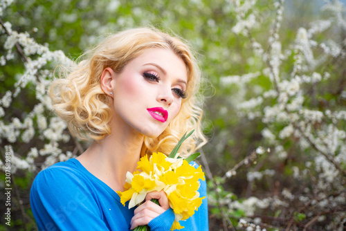 Close-up portrait of a beautiful young woman with curly blonde hair  perfect skin and beautiful make up in a pink floral summer garden.