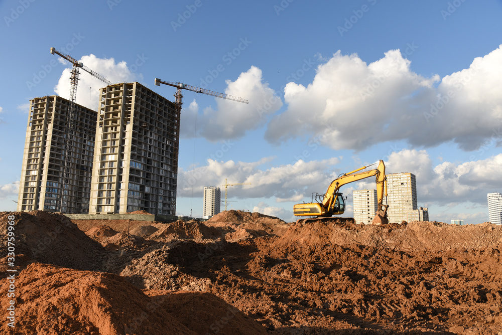 Excavator during Earthmoving Works at construction site. Backhoe digs the foundations of the building and for paving out sewer line. Construction machinery for excavating, loading, lifting and hauling Excavator during Earthmoving Works at construction site. Backhoe digs the foundations of the building and for paving out sewer line. Construction machinery for excavating, loading, lifting and hauling