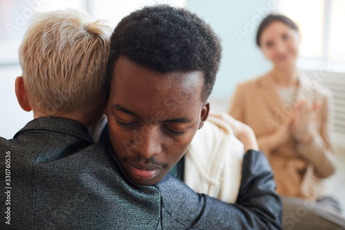 Back view of female psychologist embracing African-American teenager during therapy session in support group, copy space