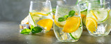 Summer healthy lemonade, cocktails of citrus infused water or mojitos, with lime lemon orange, ice and mint, diet detox beverages, in glasses on gray background. Banner