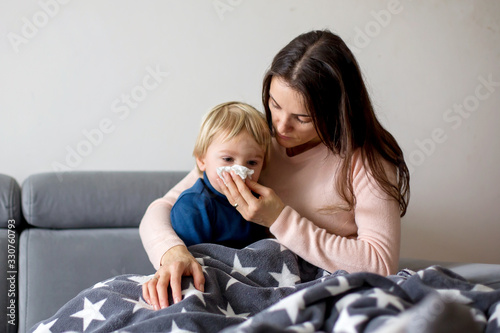 Fotografia Mother holding sick child, lying together on a couch at home with fever and runn