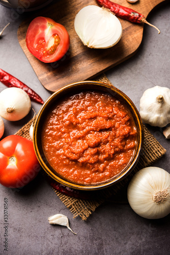 onion tomato masala or puree for indian gravy, served in a bowl with raw tamatar, pays and lehsun and red chilli, selective focus photo