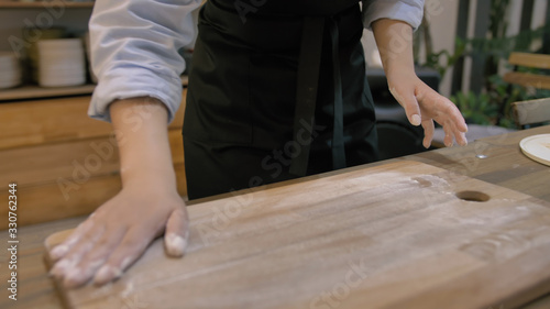 Girl in a black apron kneads the dough on a wooden cutting board close up