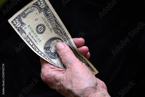 In the hands of an old woman dollar bills. Black background. Concept - Survive Retirement, Poverty