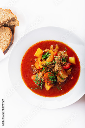 Hot beef hungarian goulash soup with paprika, beef, potatoes, carrots, onion, pepper and herbs. White background. High key. Top view.