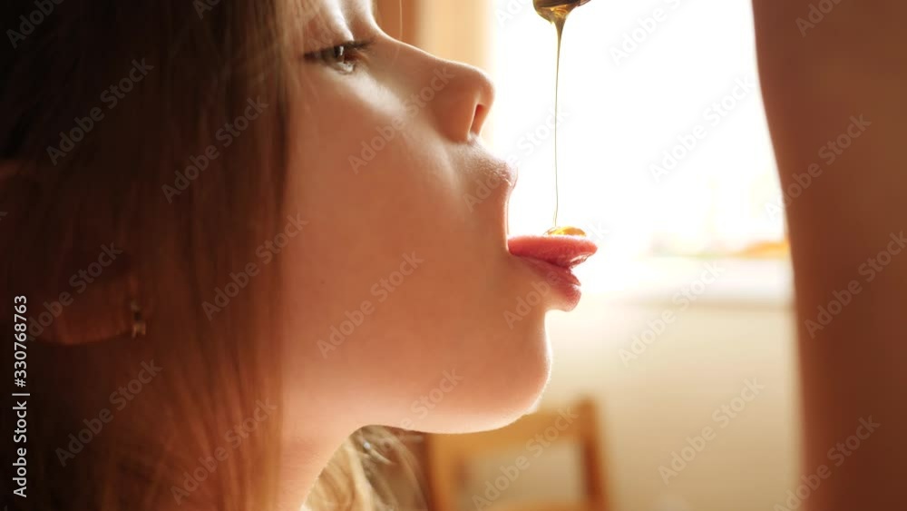 Little child girl eat honey as it drops on her tongue licking it out ...  
