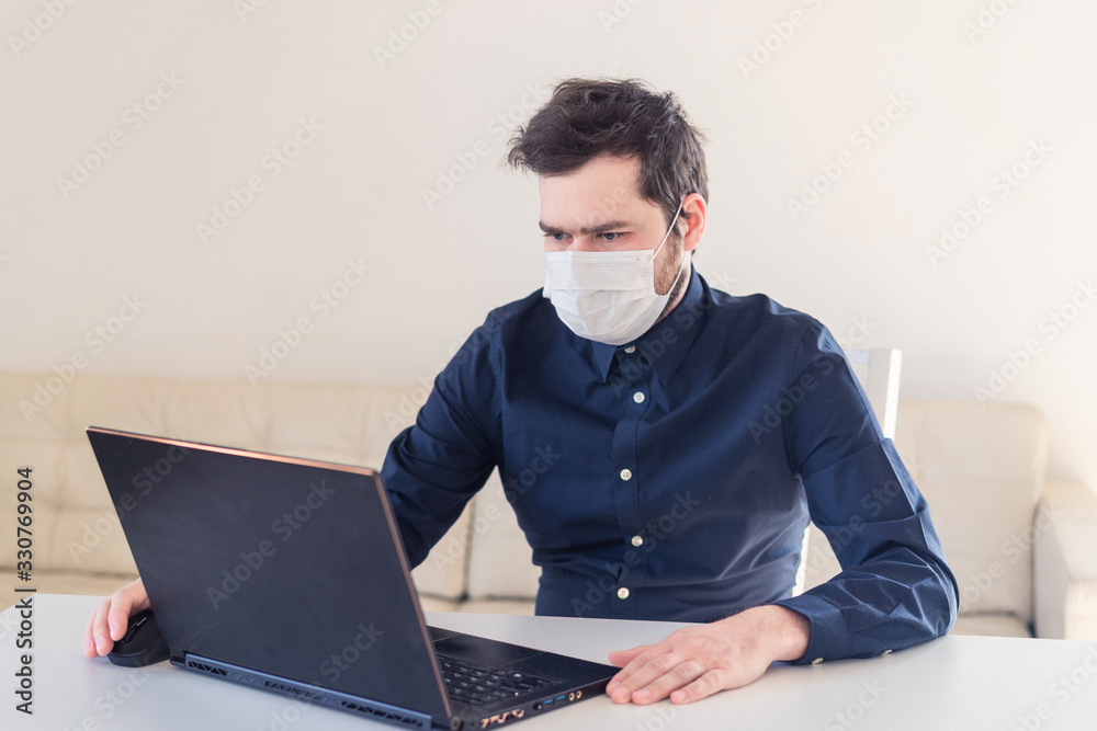 Men remote work from home behind laptop during epidemic in medical mask Men remote work from home behind laptop during epidemic in medical mask
