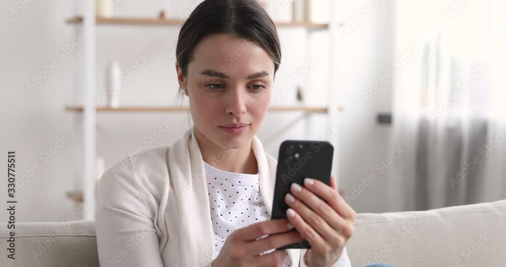 Beautiful young woman looking at smartphone surfing social media dating apps. Pretty millennial girl watching video stories, checking feed, reading news ot texting messages using mobile phone at home. Beautiful young woman looking at smartphone surfing social media dating apps. Pretty millennial girl watching video stories, checking feed, reading news ot texting messages using mobile phone at home.