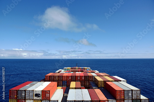 View on the containers loaded on deck of the large cargo ship. She is sailing through calm, blue ocean.  photo