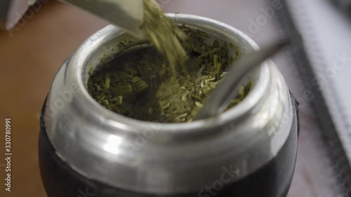 Filling mate with yerba mate leaves leaf typical infusion drink in Argentina and Uruguay with work items phone and notebook in the afternoon freelancer breakfast in office desk wood photo