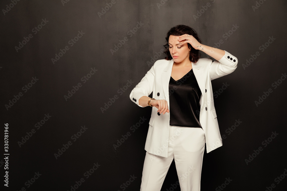 A business woman in a white suit looks at her watch over black background. Free space A business woman in a white suit looks at her watch over black background. Free space