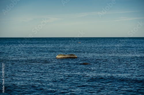 sunny beach with blue water and large rocks in the sand © Martins Vanags