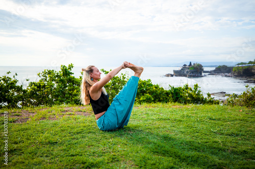 Outdoor yoga practice. Attractive woman practicing Ubhaya Padangusthasana, Wide-Angle Seated Forward Bend. Strengthen legs and core. Tanah Lot temple, Bali. photo