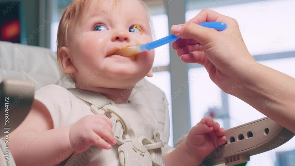 Woman feeding child with spoon. Mom feed baby with pureed food. Mom feeding kid in baby chair