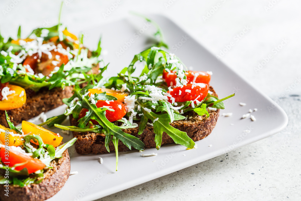 Tomatoes, arugula and cheese sandwiches on a gray plate.