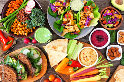 Healthy lunch table scene with nutritious Buddha bowl, lettuce wraps, vegetables, sandwiches and salad. Above view over a wood background. photo