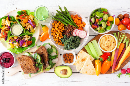 Healthy lunch table scene with nutritious lettuce wraps, Buddha bowl, vegetables, sandwiches, and salad. Overhead view over a white wood background.