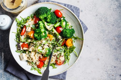 Vegan quinoa salad with tofu, broccoli, tomatoes and nutty dressing. Healthy food concept.