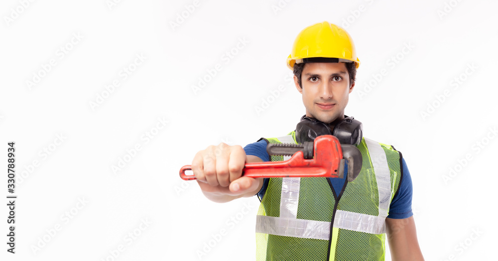 Portrait young handyman standing, holding adjustable wrench and showing tool, isolated white background, copy space. Successful worker or repairman wearing safety helmet safety vest, ready fix service