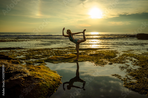 Outdoor sunset yoga. Attractive woman practicing yoga, standing in Natarajasana, Lord of the Dance Pose. Amazing water reflection. Bali, Indonesia