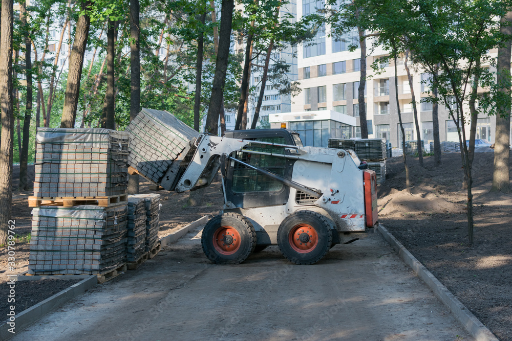 A small loader works in the park and carries piles of paving slabs. Works on improvement in the park.