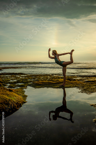 Outdoor sunset yoga. Attractive woman practicing yoga, standing in Natarajasana, Lord of the Dance Pose. Amazing water reflection. Bali, Indonesia