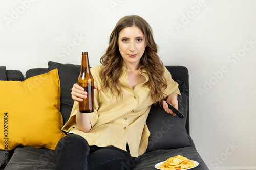 Картината върху платно A young woman sits at home on the couch and watches TV alone.